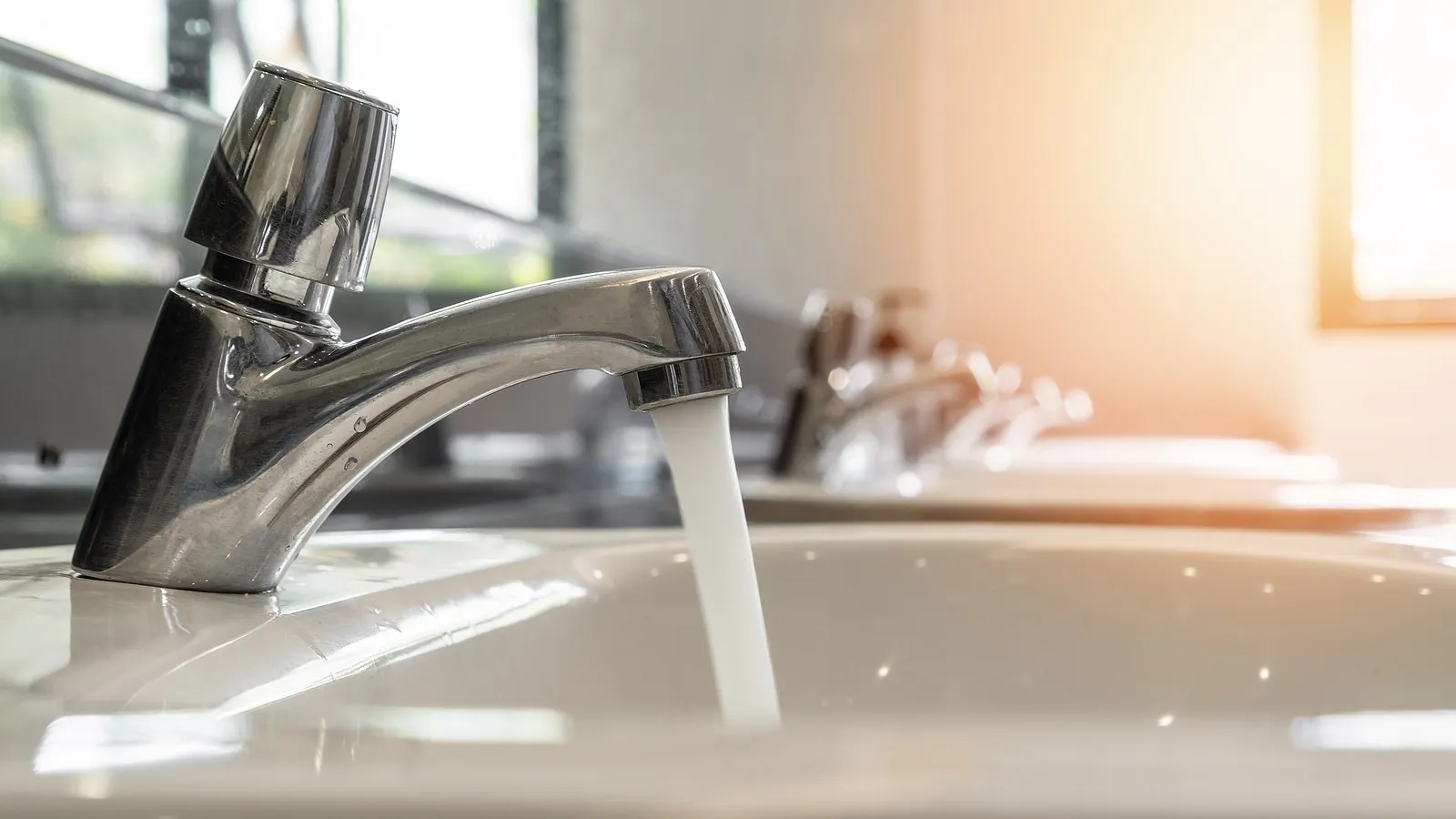 Modern chrome bathroom faucet running into a white sink basin
