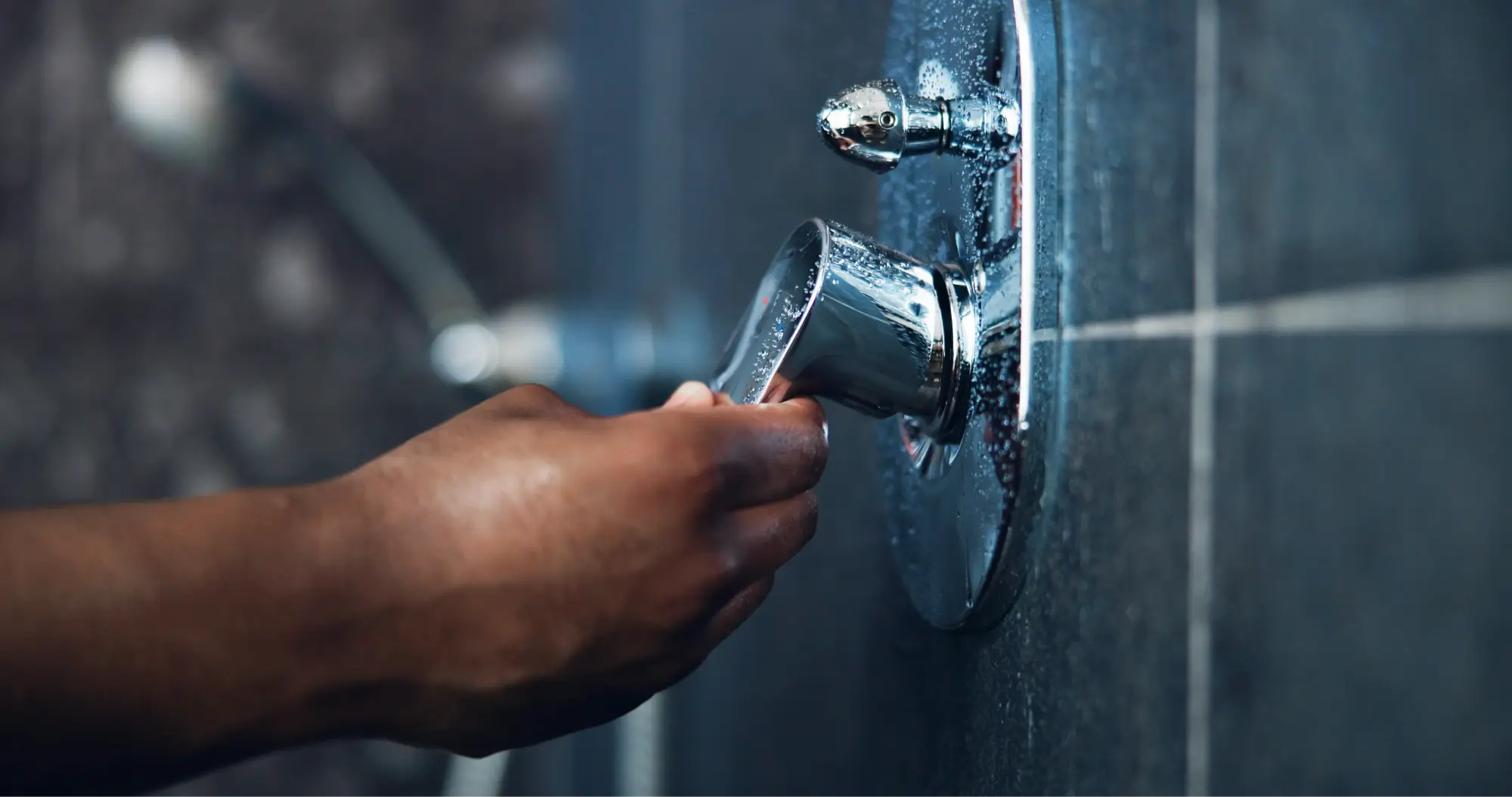 Hand adjusting chrome shower hardware on a tiled shower wall